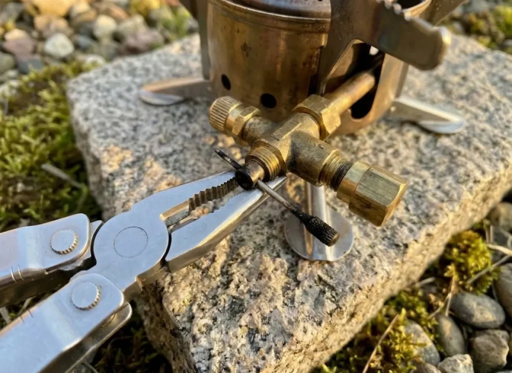 Close-up of pliers gripping the brass components of an MSR Dragonfly stove during field maintenance.