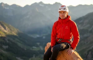 Test Handholds for Stability Before Committing Weight A professional scrambler in a red Arc'teryx jacket carefully assessing a sandstone fin on an exposed ridge during golden hour.