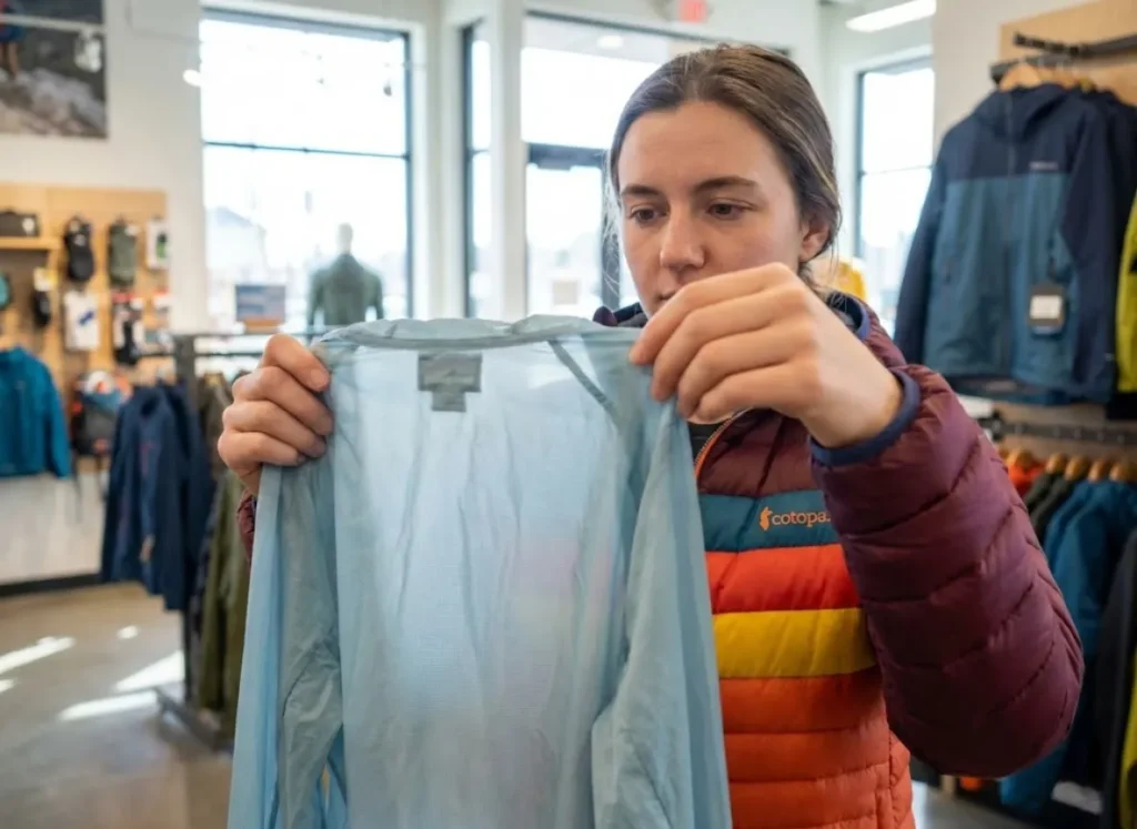Shopper testing wind shirt fabric breathability CFM in outdoor gear store