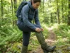 Ticks, Gaiters & Hiking: The 3-Stage Defense System Hiker adjusting Outdoor Research gaiters on a forest trail to prevent tick bites while hiking