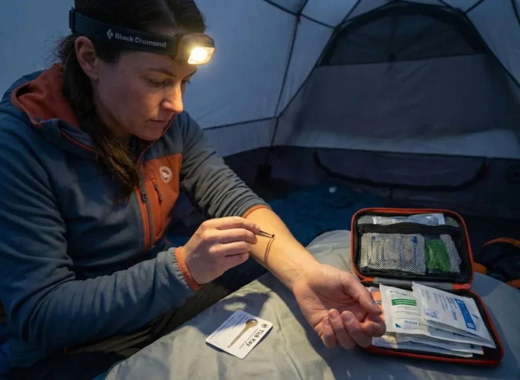 Hiker using fine-tipped tweezers to remove a tick inside tent with headlamp for visibility