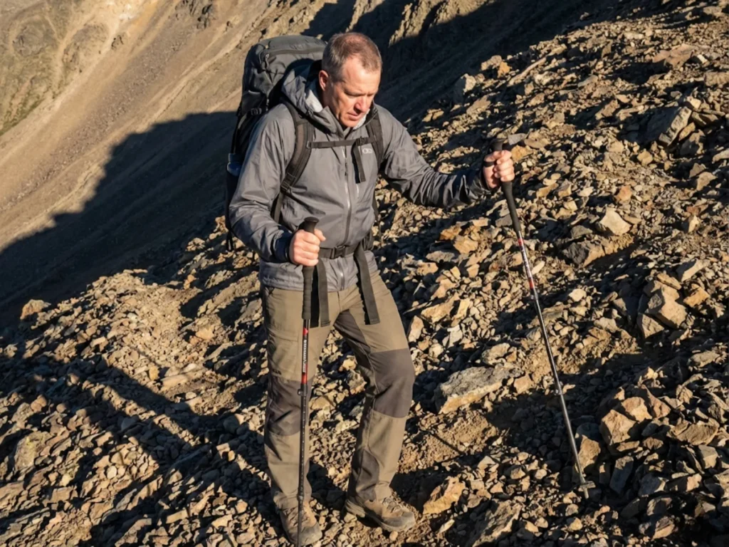 Hiker descending steep scree slope using trekking poles for stability and load distribution