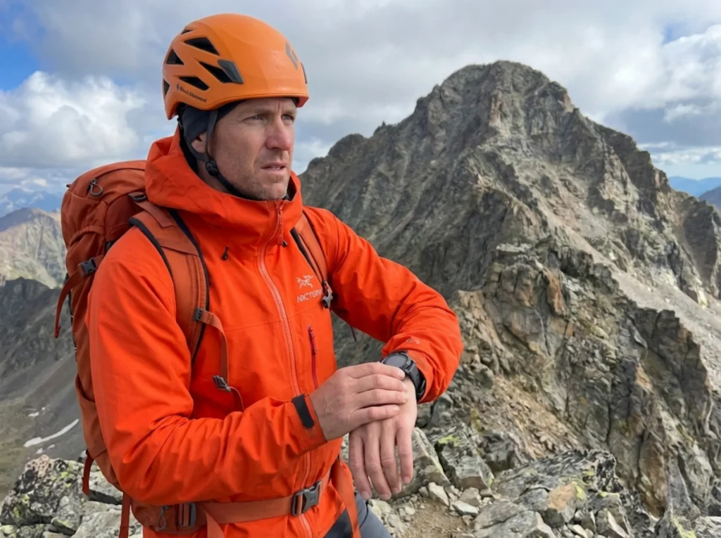 Mountaineer checking GPS watch on alpine ridge deciding turnaround time for summit attempt