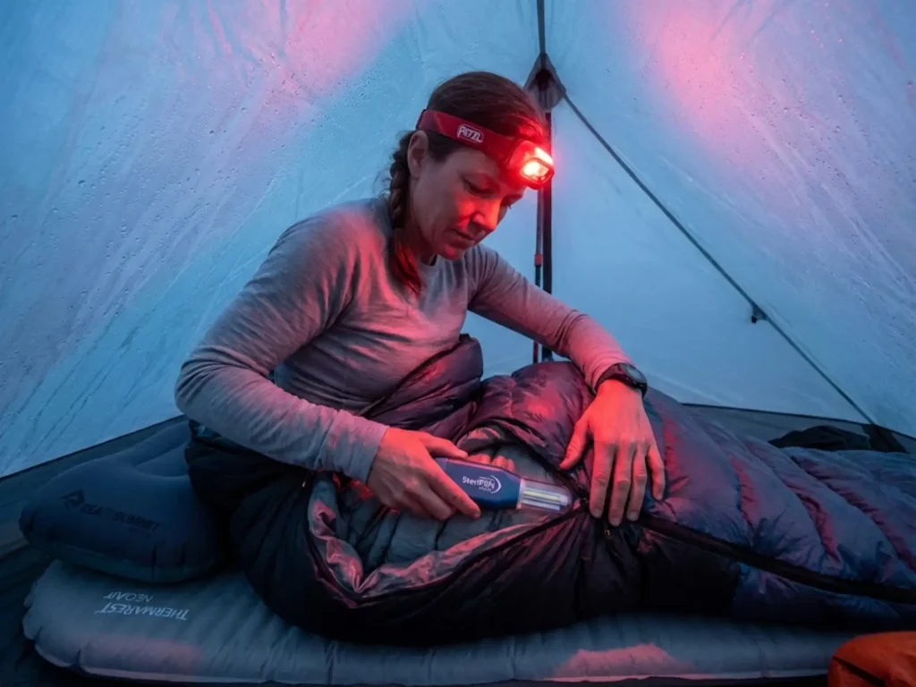 Thru-hiker retrieving UV water purifier kept warm inside sleeping bag on cold morning