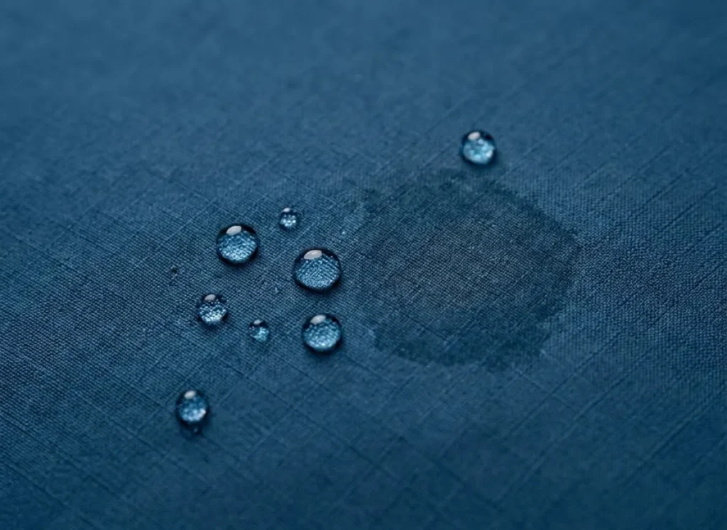 Extreme macro close-up of water droplets beading on the surface of a blue Gore-Tex Pro jacket fabric, illustrating DWR performance and textile texture.
