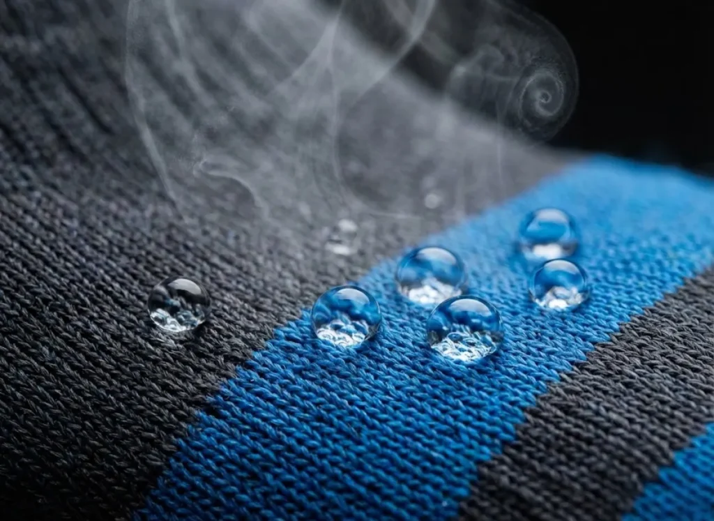 Macro close-up of waterproof sock fabric weave with water droplets beading on top and subtle vapor rising to illustrate breathability.