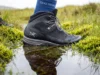 Waterproof Socks Trap Sweat Inside Your Boots Close-up of a high-end hiking boot stepping into water, highlighting the texture of a waterproof sock cuff and water beading technology.