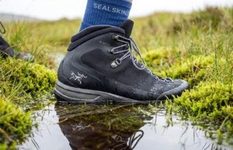 Waterproof Socks Trap Sweat Inside Your Boots Close-up of a high-end hiking boot stepping into water, highlighting the texture of a waterproof sock cuff and water beading technology.