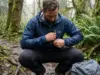 Packable vs Ultralight Rain Jacket Which Wins Hiker stuffing an ultralight rain jacket into its own pocket on a wet Olympic Peninsula trail