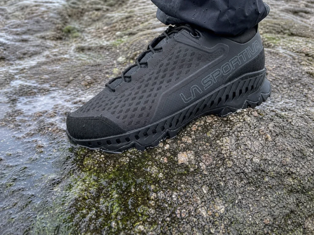 Close-up of a hiking shoe sole compressing against wet textured rock showing rubber deformation