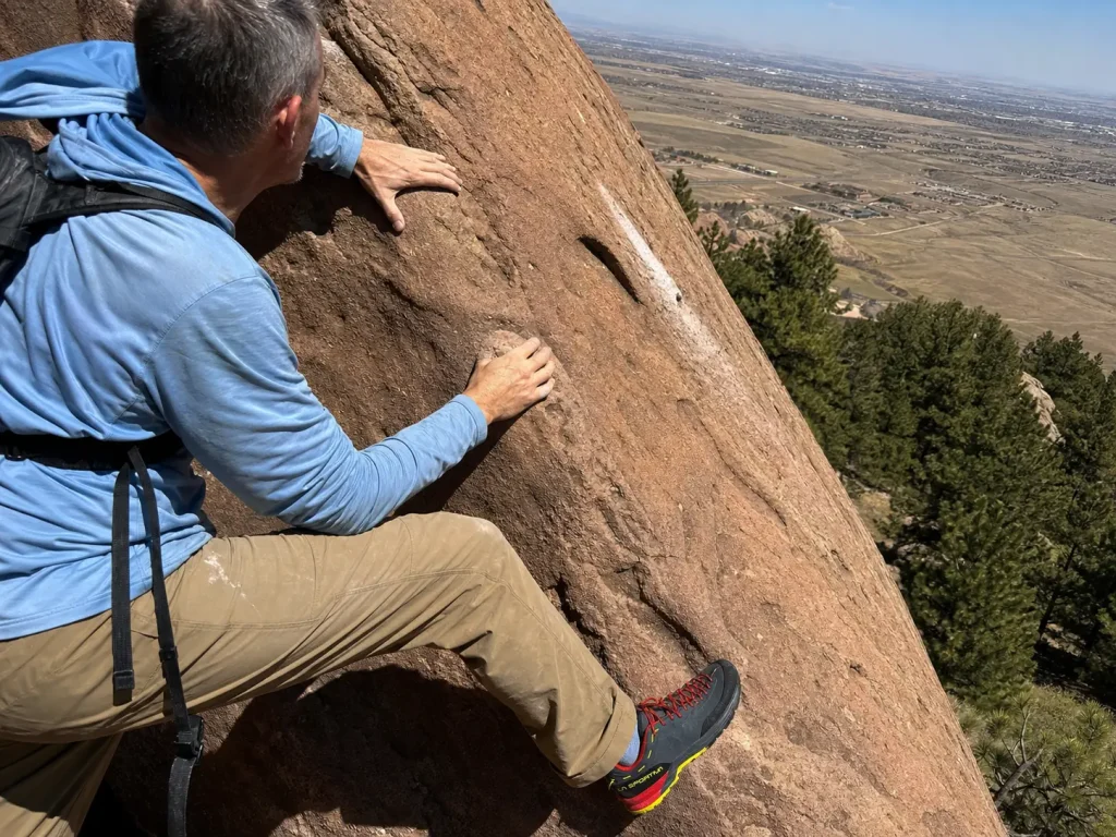 Scrambler edging an approach shoe on class 3 Flatirons rock with one hand on a sandstone hold