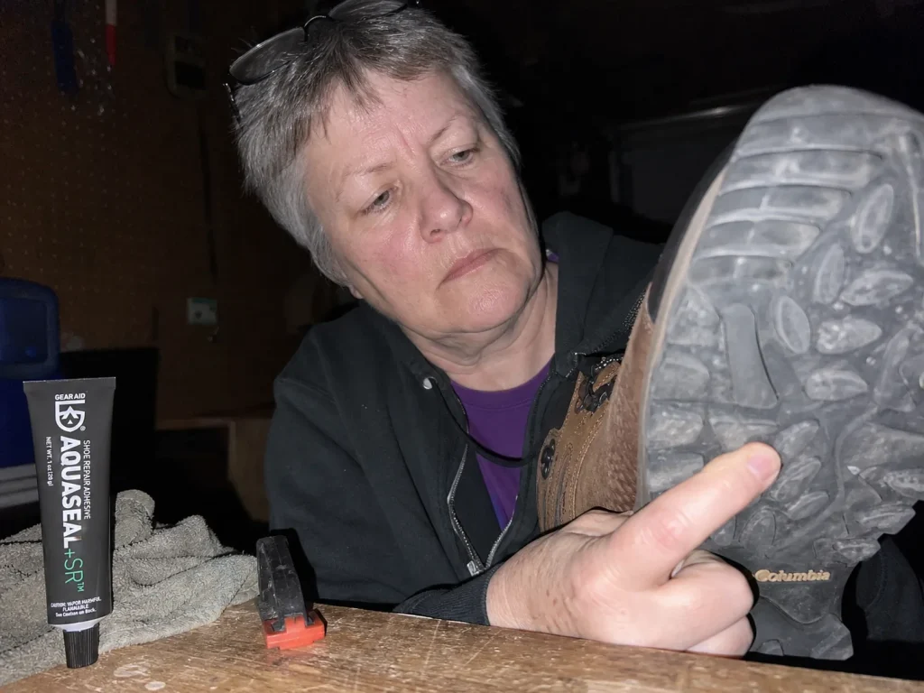 Aged hiking boot outsole with hardened rubber next to shoe repair adhesive on a garage bench