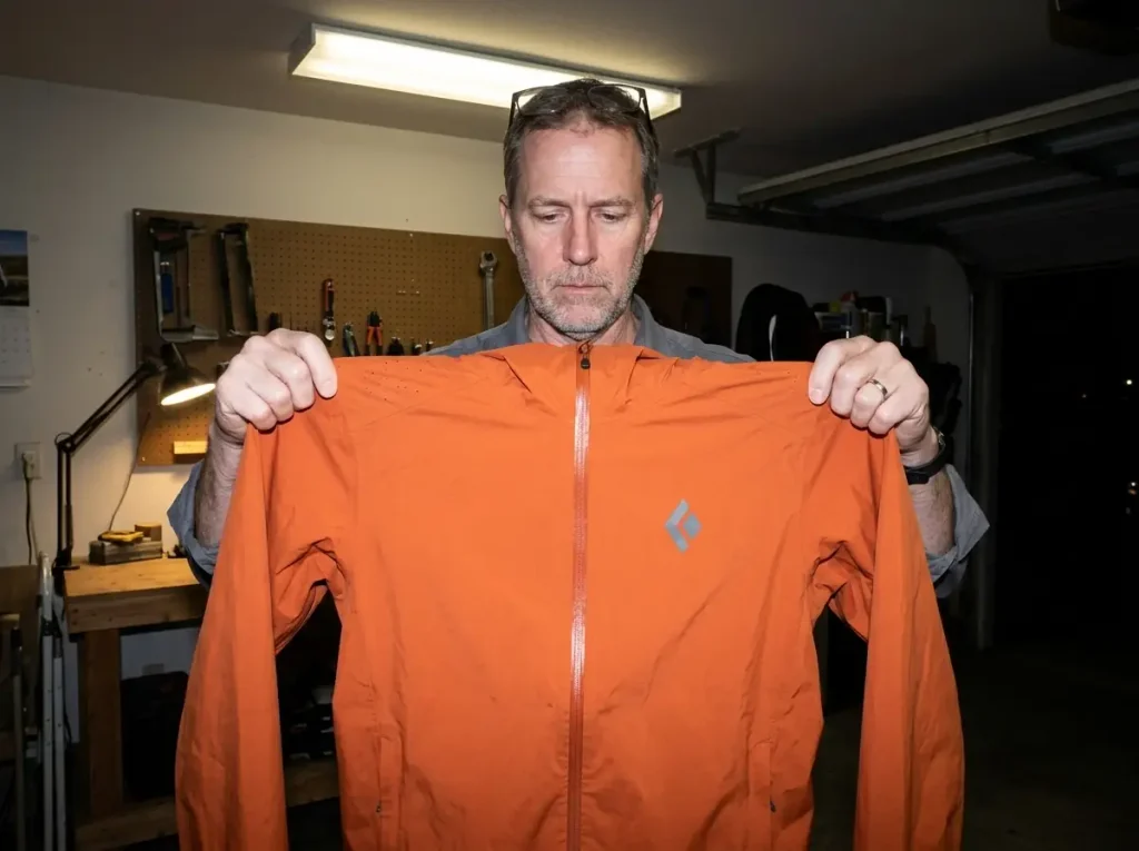 Pinhole abrasion damage on the shoulder of a rain jacket held up to the light at home