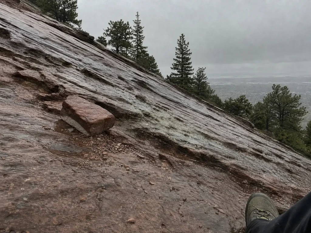 Wet Flatirons sandstone slab and loose rock under a darkening sky, the moment to turn back