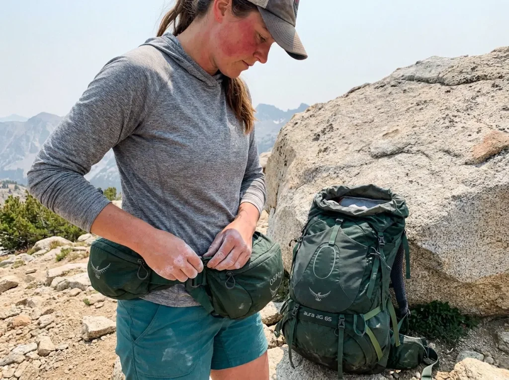 Hiker clipping a detached Osprey Aura lid to her hip belt as a summit fanny pack
