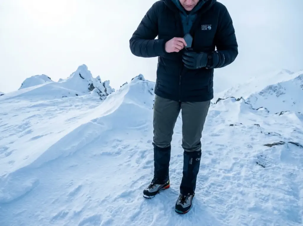 Mountaineer retrieving phone from warm internal pocket during cold weather GPS navigation