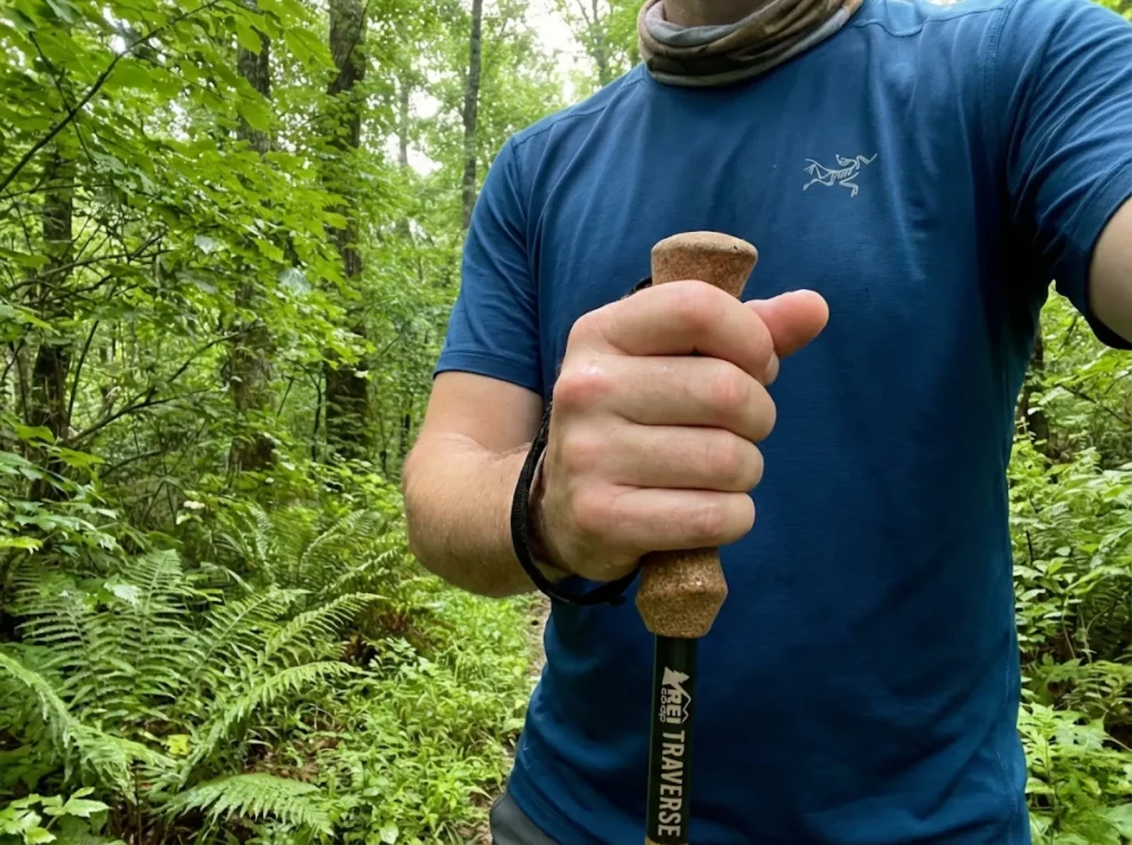 Close-up of a sweaty hand gripping a cork trekking pole handle on a humid forest trail