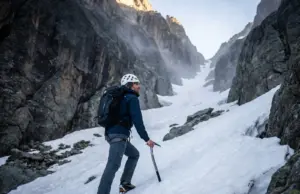 The One-Hour Window That Makes Couloir Crossings Safe Mountaineer crossing steep alpine couloir at dawn wearing Petzl helmet and crampons for rockfall safety
