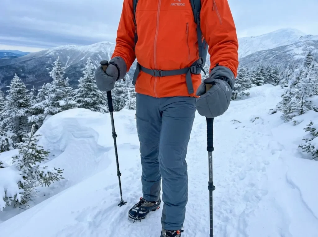 Hiker gripping EVA foam trekking poles with winter gloves on a snowy ridge