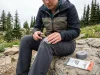 Why Most Hiking Pants Patches Peel Off in a Week Woman applying Tenacious Tape patch to torn hiking pants on alpine trail — field repair guide