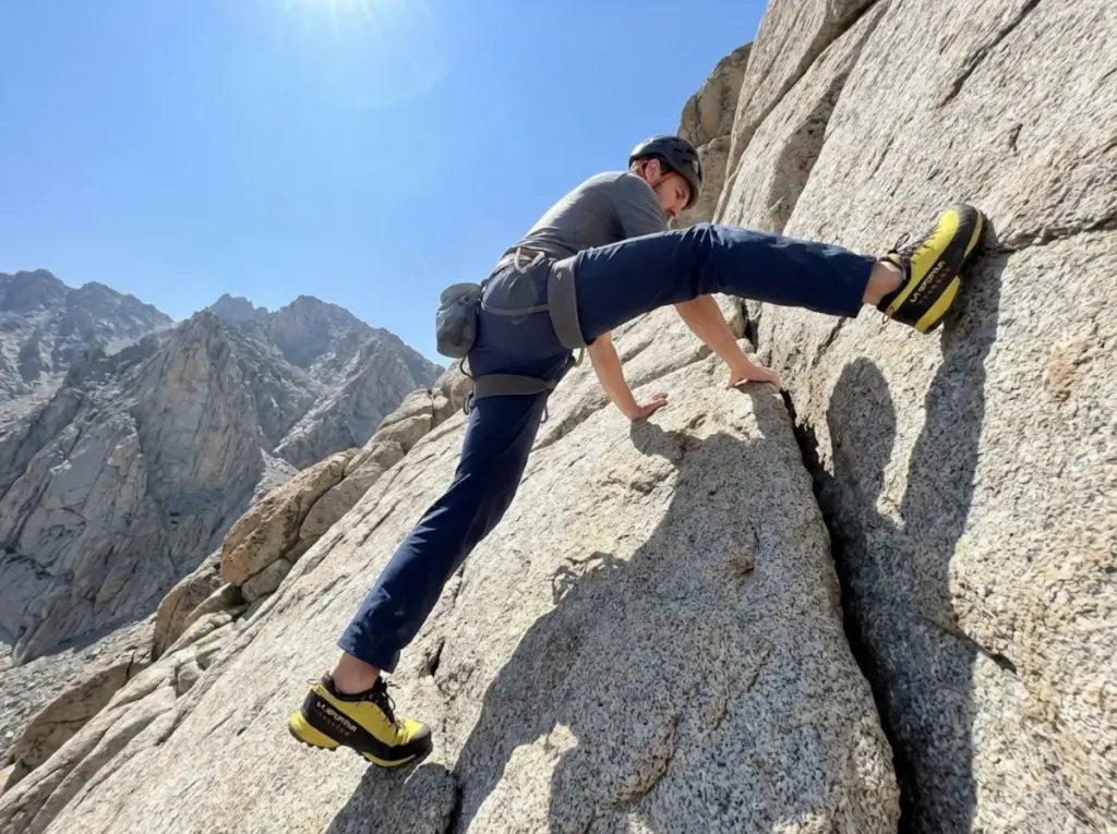 Climber performing high step on granite scramble with fitted hiking pants for visibility