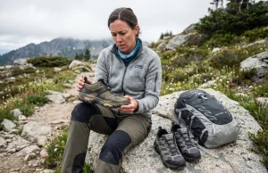 Why Your Hiking Shoes Die Early (And How to Fix It) Hiker examining worn hiking shoe midsole on alpine trail with replacement pair nearby