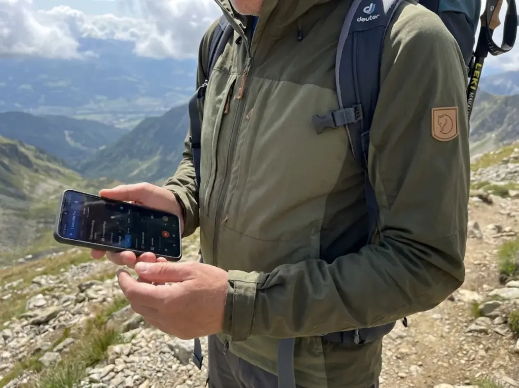 Hiker adjusting GPS app recording interval settings on mountain trail switchback