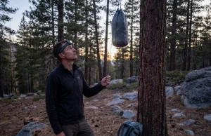 Your Bear Bag PCT Hang Is Wrong and Here’s Why Hiker evaluating PCT bear bag hang on lodgepole pine at dusk in the Sierra Nevada