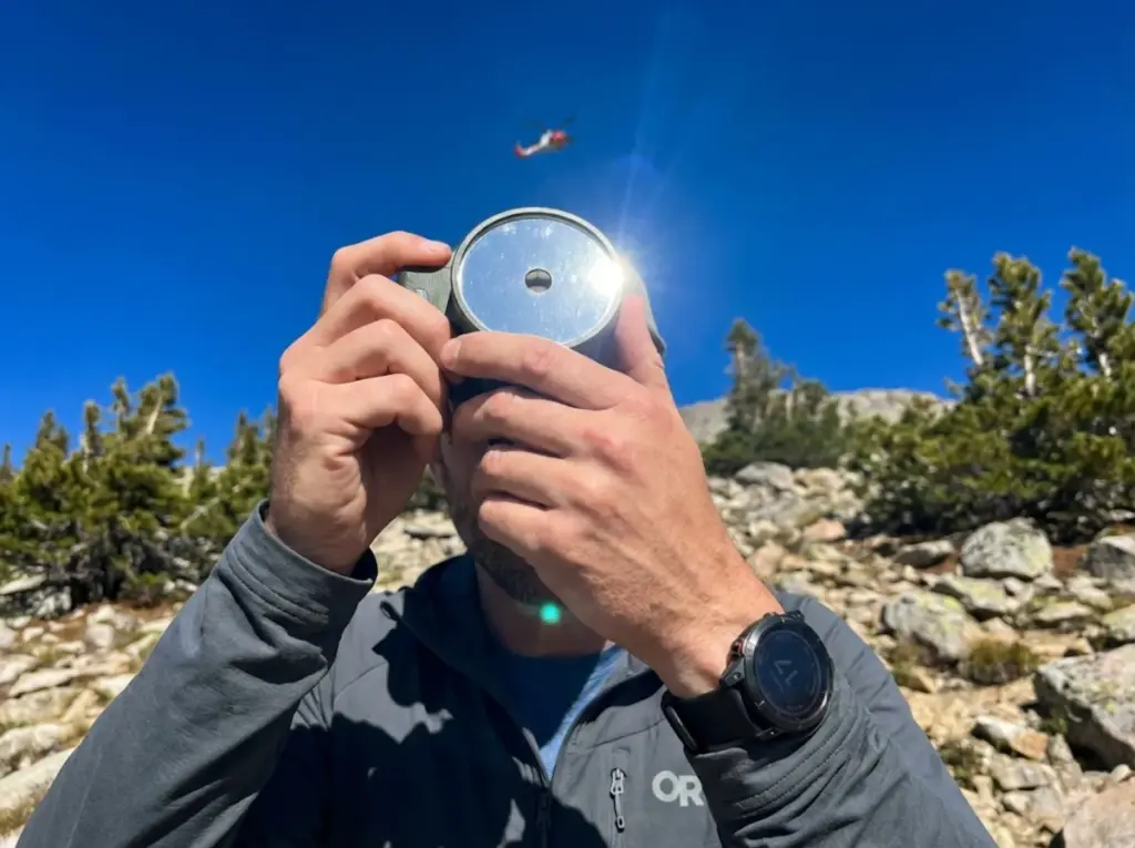 Close-up of hands aiming a military signal mirror at a rescue helicopter