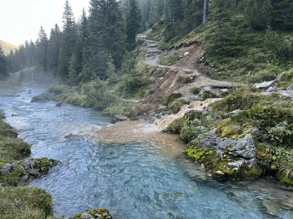 Trail erosion sediment flowing into alpine stream showing watershed contamination 