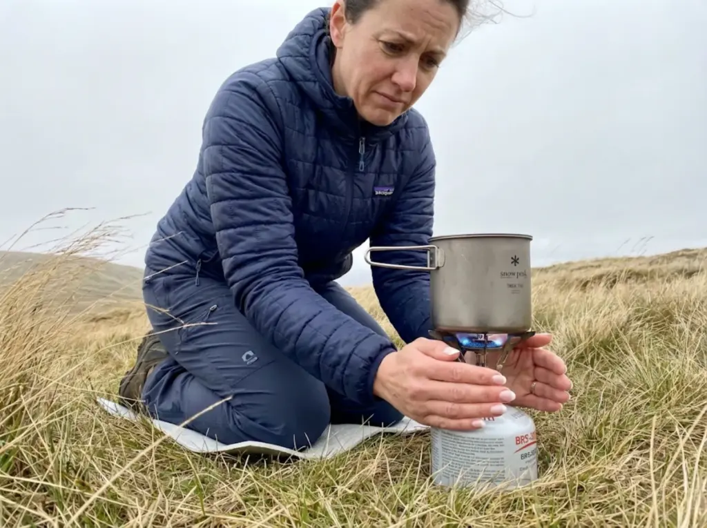 Hiker shielding BRS-3000T stove from wind on exposed mountain pass