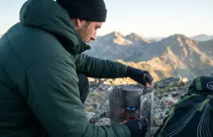 I Ran the Numbers on Windscreen Weight vs Fuel Saved Backpacker adjusting titanium windscreen around canister stove on alpine ridge