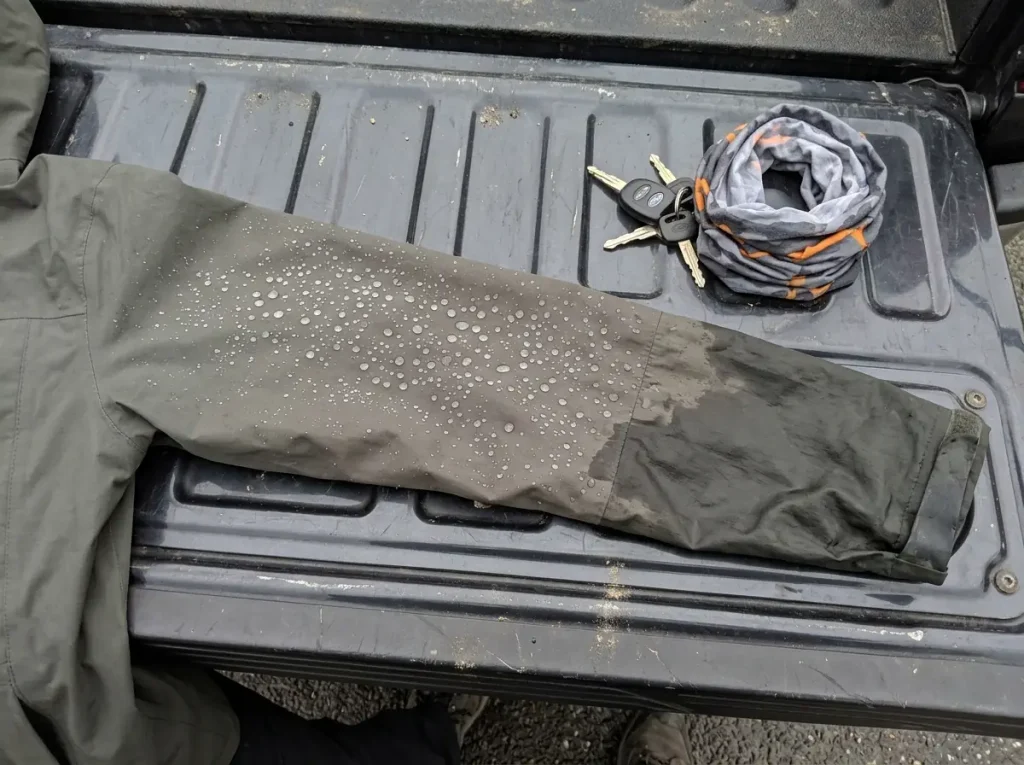 Close-up of a rain jacket sleeve where water beads on clean fabric and soaks into a worn patch