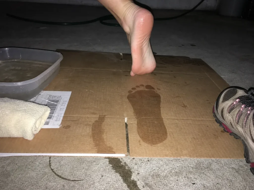 Wet footprint on cardboard from the wet-foot test, showing the flat foot shape before buying shoes