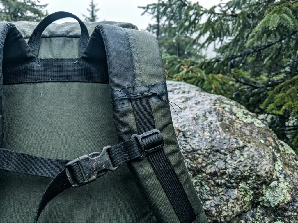 Close-up of wet backpack shoulder straps and seams, the spots that leak first before any waterproofing