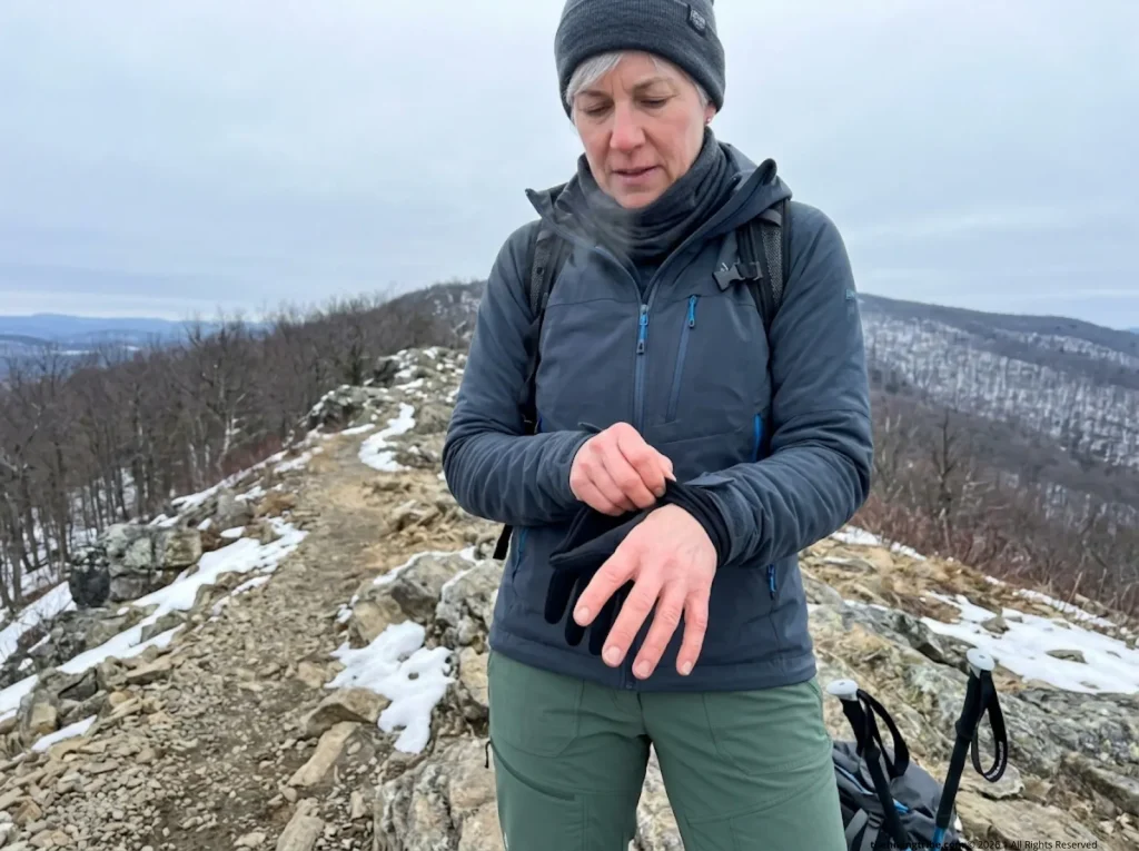 Hiker adding liner gloves to prevent extremity heat loss on cold shoulder season