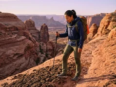 What Most Hikers Get Wrong in Fragile Ecosystems Female hiker pausing on desert canyon trail to avoid stepping on biocrust — how to hike in sensitive ecosystems safely