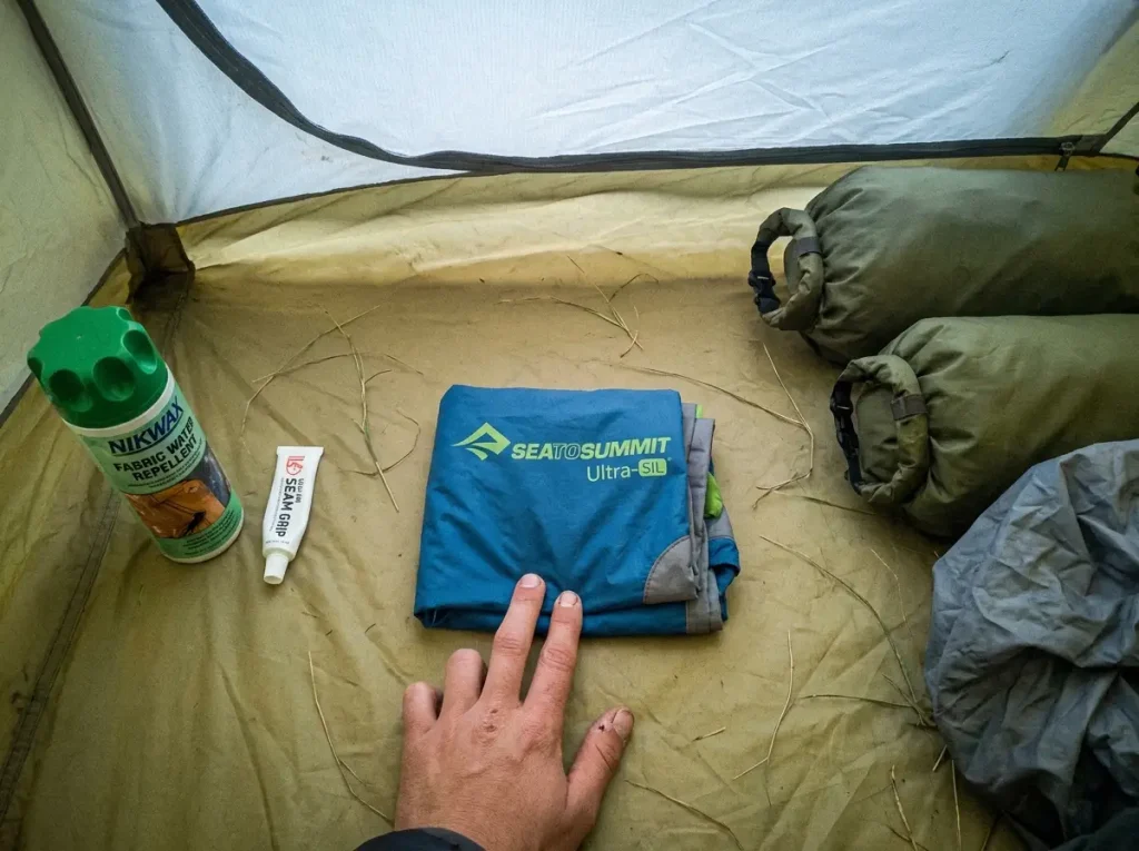 Backpack waterproofing layers laid out in order: DWR spray, seam sealer, pack liner, dry bags, rain cover