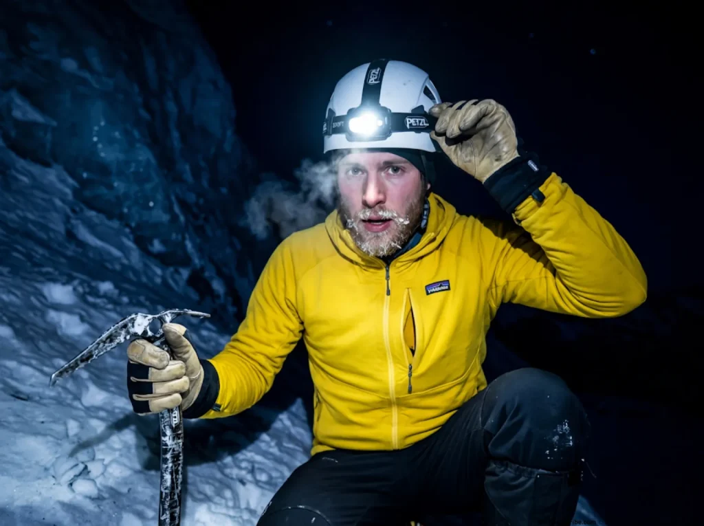 Mountaineer adjusting headlamp during pre-dawn alpine start on steep glacial ice