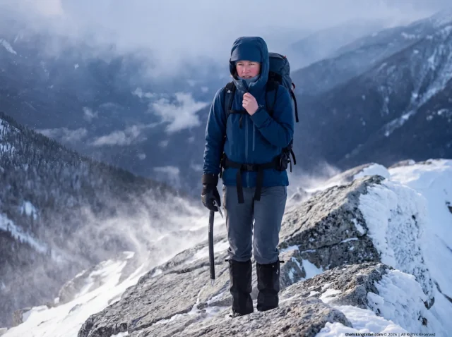 prevent-frostbite-winter-hike-ridge Female hiker adjusting jacket to prevent frostbite on a frozen winter ridge