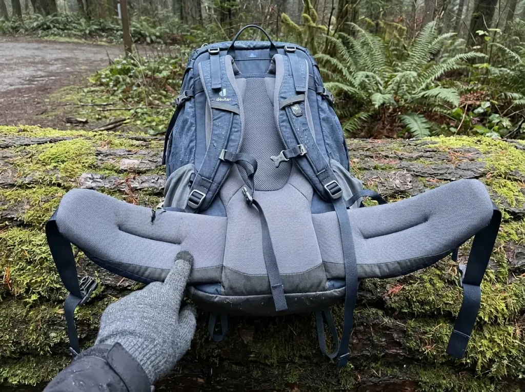 Internal-frame backpack laid open on a log showing hip belt, shoulder harness and back panel