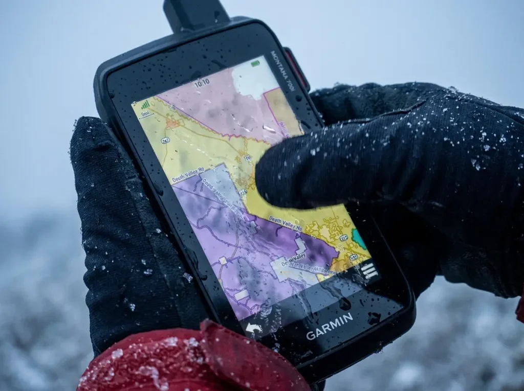 Gloved hand struggling with a touchscreen hiking GPS in sleet showing cold-weather touchscreen failure