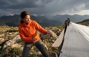How to Set Up a Tarp Shelter for Hiking Without Trees Female hiker setting up a flat tarp shelter with trekking poles in an exposed treeless alpine environment before a storm