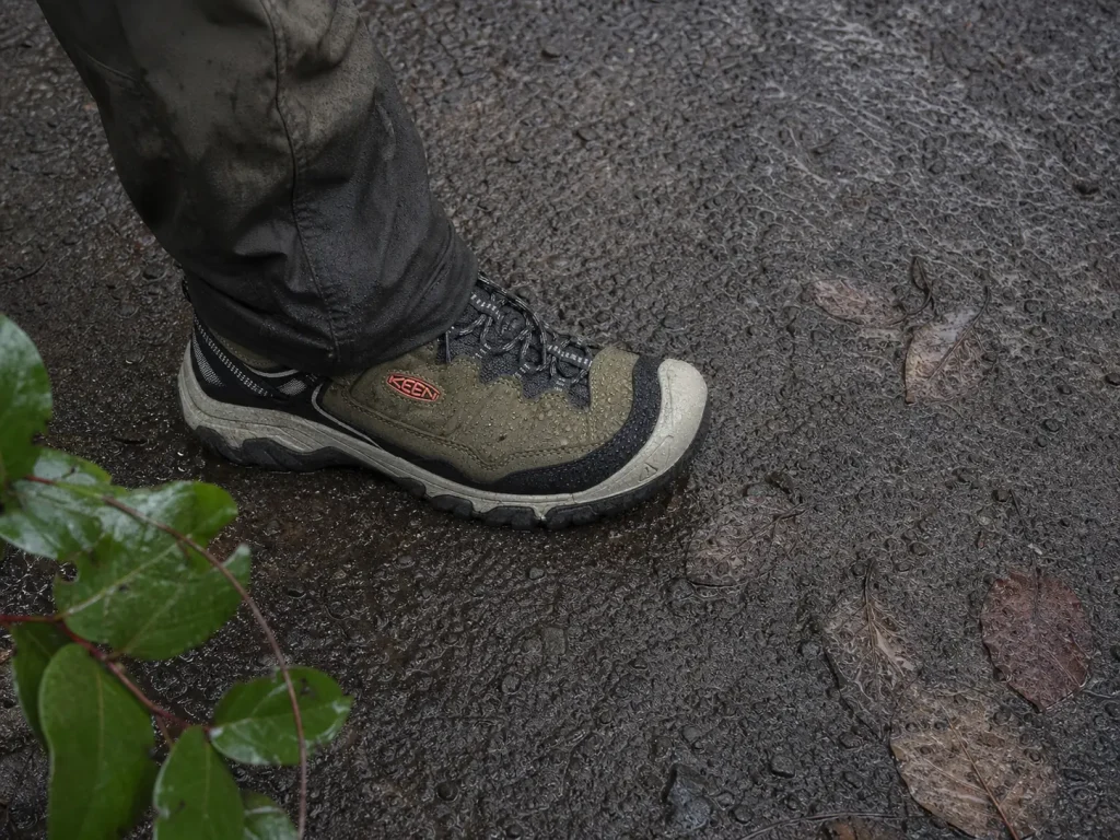 Waterproof low-cut hiking shoe beading rain on a wet trail, showing membrane breathability limits