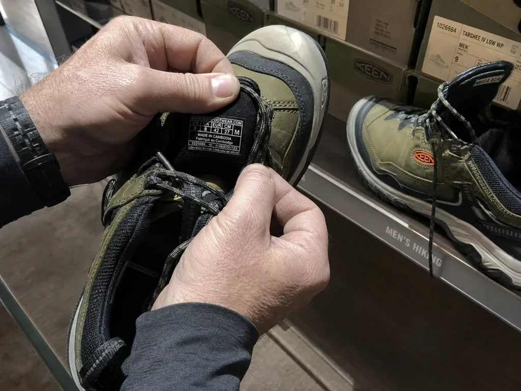 Hands checking the width label inside a KEEN Targhee 4 hiking shoe before buying