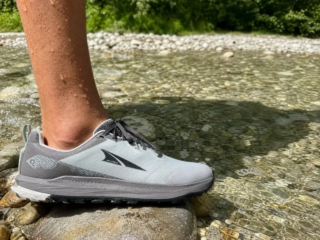 Low-cut trail running shoe at the edge of a shallow creek crossing on a bright summer day