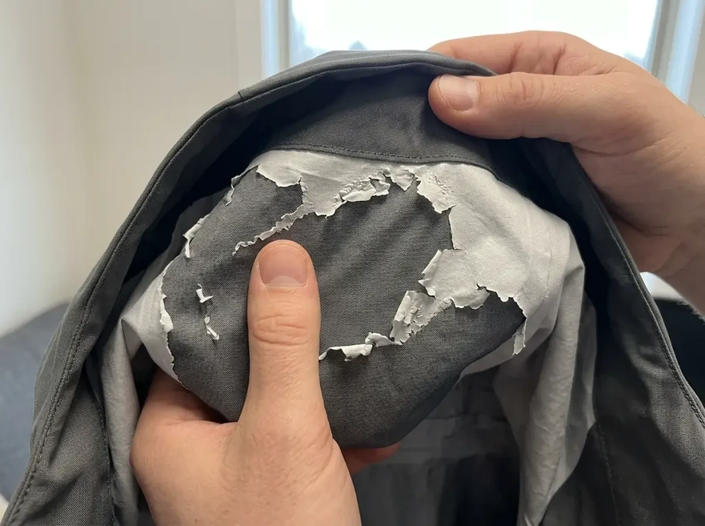 Peeling white membrane inside a rain jacket hood showing delamination damage