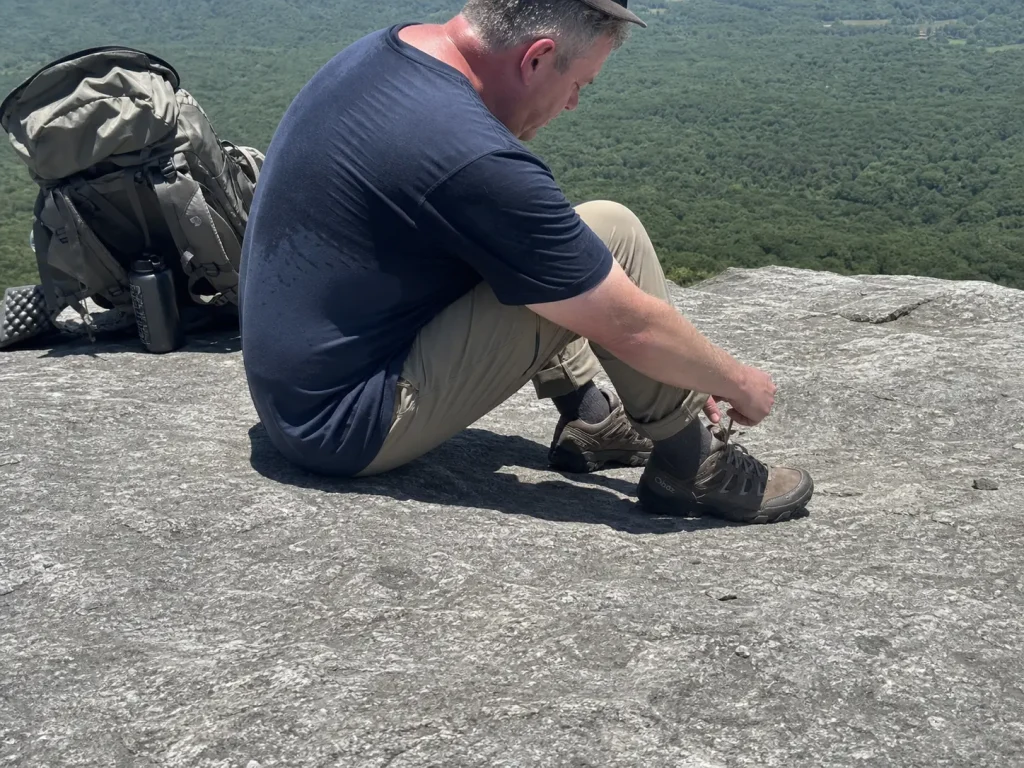 Hiker loosening his laces at a midday break as his feet swell inside his hiking shoes
