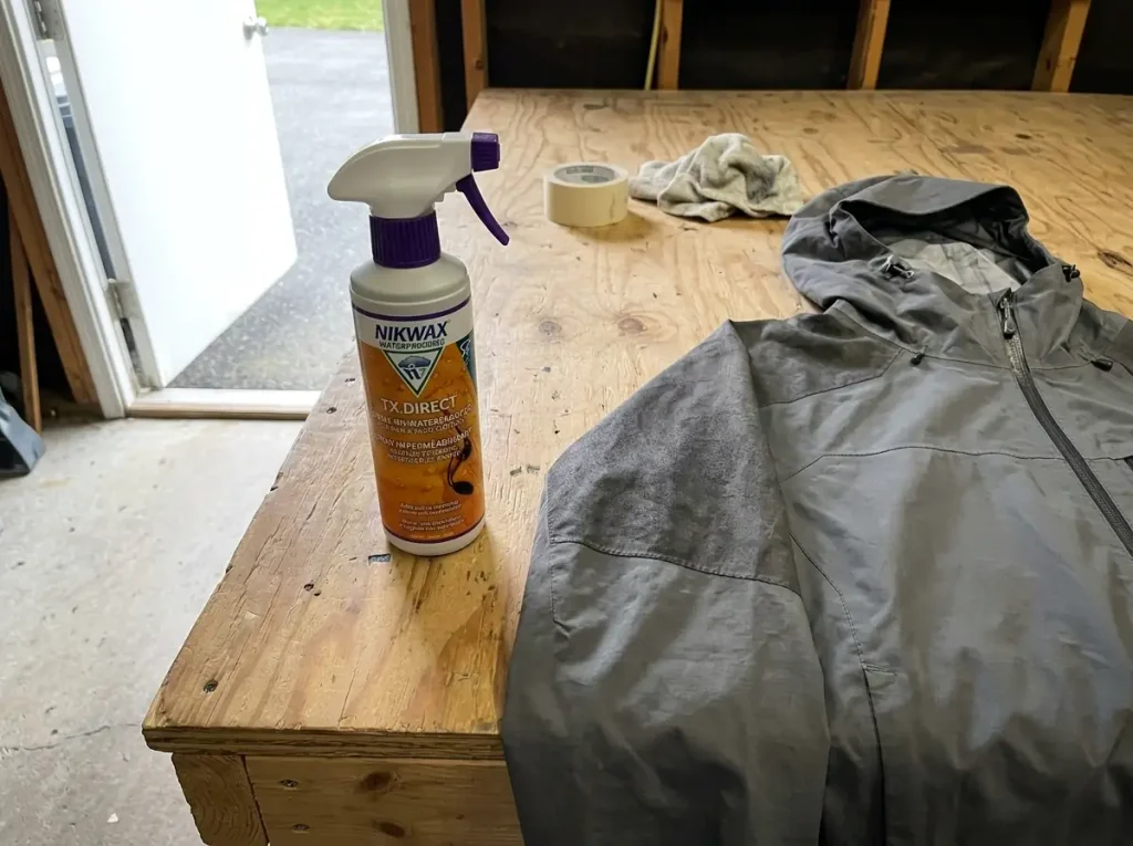 Nikwax reproofing spray beside a worn rain jacket on a garage bench