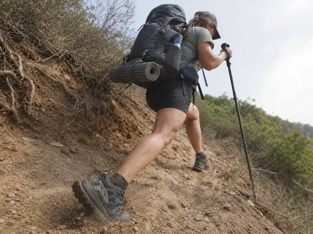 Backpacker with a loaded pack descending a steep trail in minimalist shoes